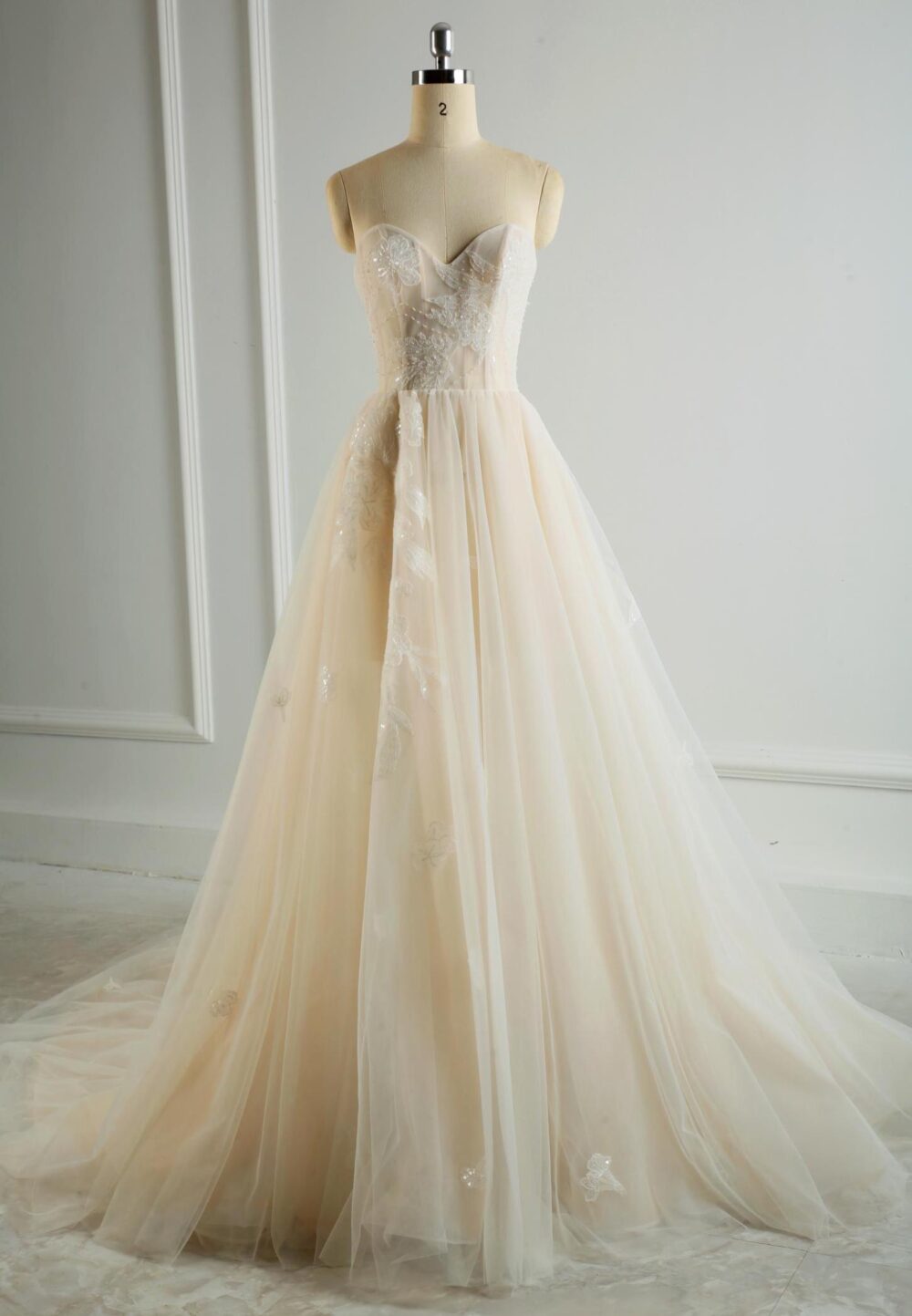Ethereal strapless A-line wedding dress with a lace bodice and flowing champagne tulle skirt, perfect for a romantic wedding.