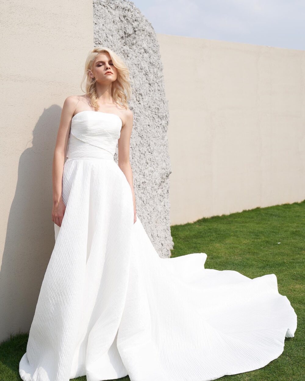 Modern strapless textured ball gown wedding dress with an asymmetrical pleated bodice and statement blush satin bow.