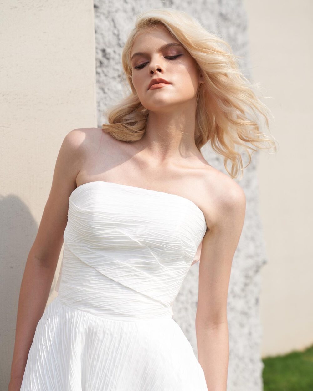 Modern strapless textured ball gown wedding dress with an asymmetrical pleated bodice and statement blush satin bow
