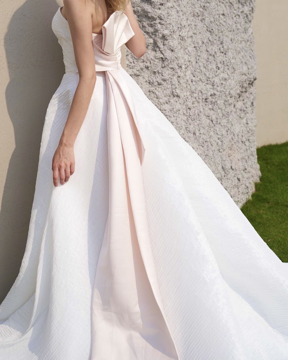 Modern strapless textured ball gown wedding dress with an asymmetrical pleated bodice and statement blush satin bow
