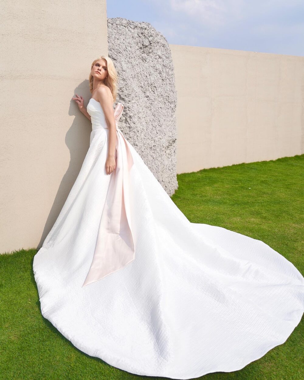 Modern strapless textured ball gown wedding dress with an asymmetrical pleated bodice and statement blush satin bow